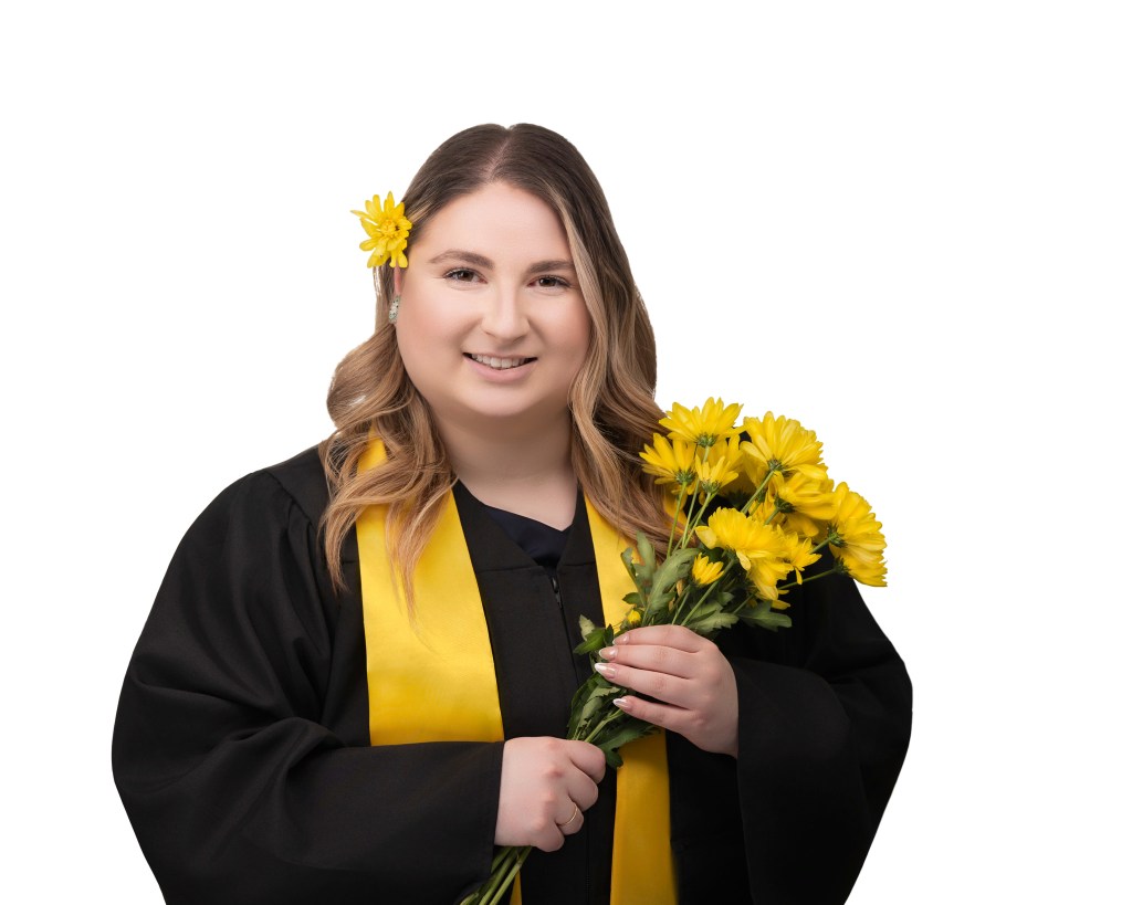Graduation Headshot subject holding a bundle of yellow flowers, one flower in her hair and she is wearing a black gown with a yellow stole